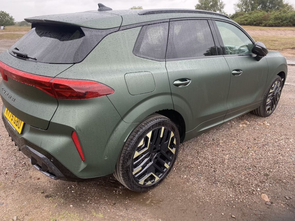 A green SUV parked on gravel, featuring a sleek design and shiny black wheels, with raindrops on the surface.